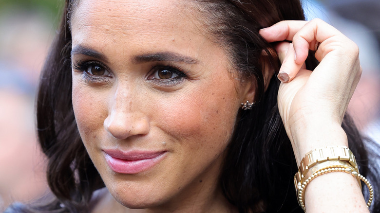 Meghan Markle puts hair behind ear in black dress