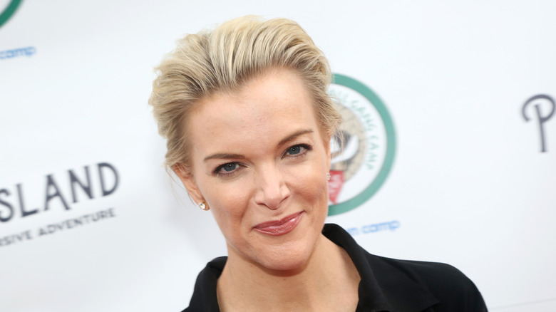Megyn Kelly in a black shirt smirking at the camera in 2019 with short blond hair