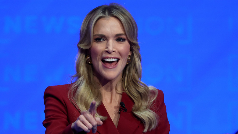 Megyn Kelly on stage in a red blazer with longer hair in 2023