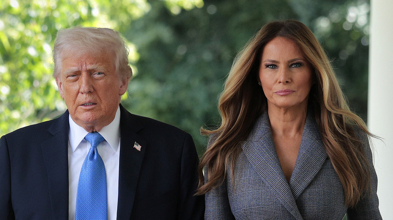 Donald Trump wearing a suit and blue tie walking with Melania Trump, who's wearing a gray blazer and skirt.