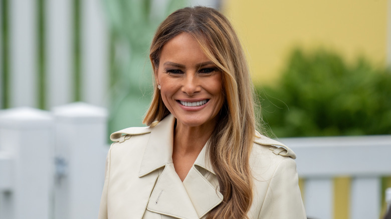 Melania Trump smiling outdoors with a blurred background