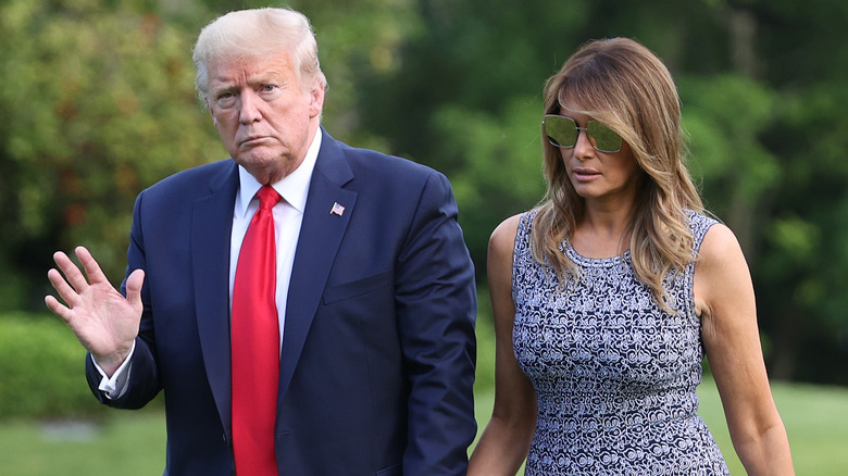 Donald Trump in a navy suit and Melania Trump in a black and white patterned dress photographed as they return to the White House