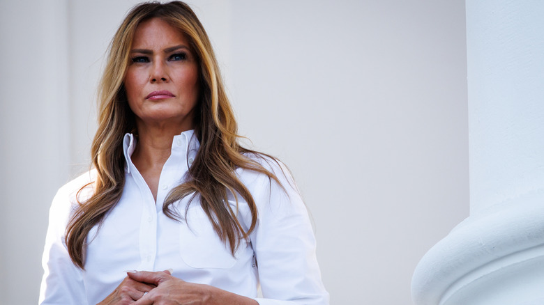Melania Trump frowning in a white shirt while standing on balcony