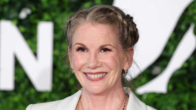 Melissa Gilbert smiling while posing in a white jacket with her hair in a twisty updo
