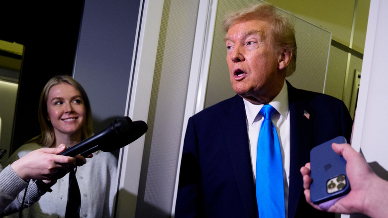 Karoline Leavitt smiles and looks at Trump as he leans through a door way to address reports.
