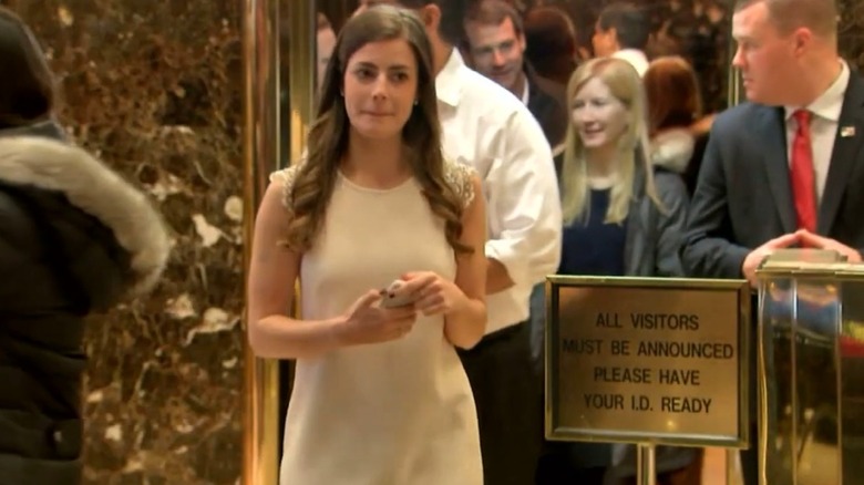 Madeleine Westerhout wears a white dress while holding her phone inside Trump Tower.