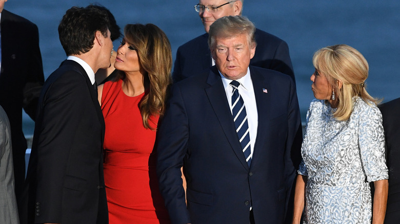 Justin Trudeau and Melania Trump exchange an air kiss beside a squinting Donald Trump as Brigitte Macron looks on.