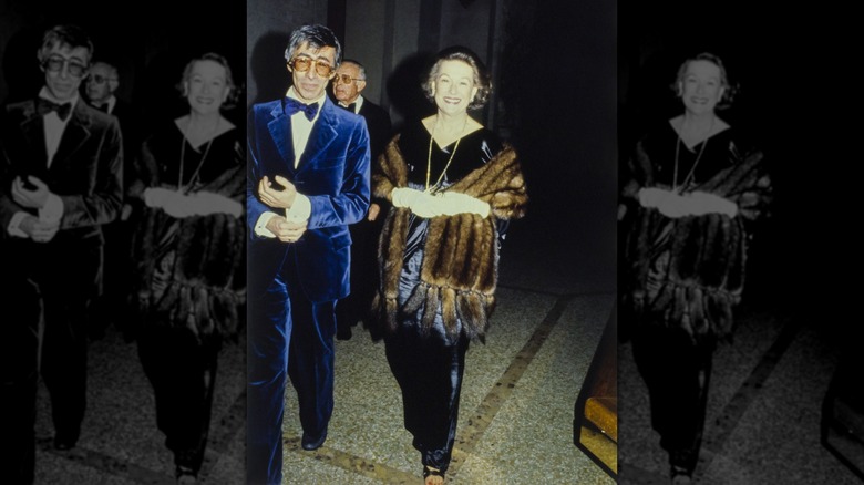 Jan Cowles (right) wearing a black satin gown with a fur wrap edged with tails, escorted by a man in a blue velvet suit (left), at the Metropolitan Museum of Art Gala
