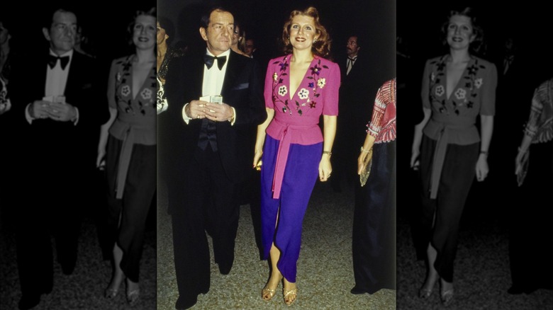 Unidentified woman dressed in a pink wrap blouse and purple skirt, walking with an unidentified man in a tuxedo at the 1979 Met Gala