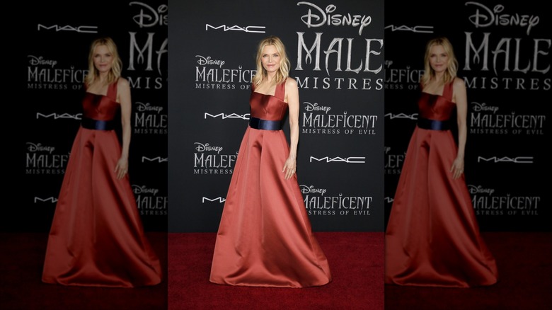 Michelle Pfeifer on the Maleficent red carpet in a floor length rust-colored dress with a navy satin belt at the waist
