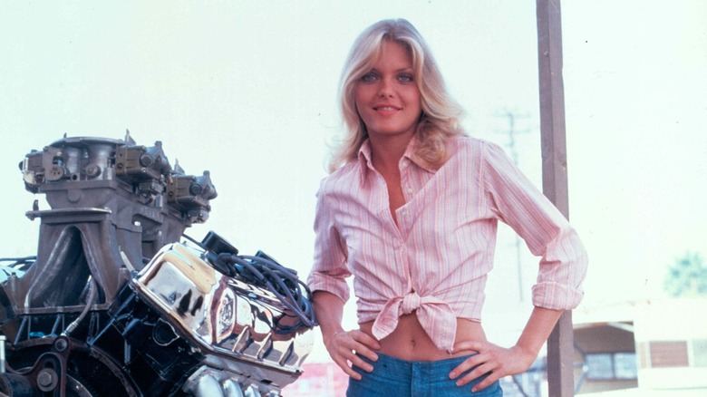 Michelle Pfeiffer with hands on hips in pink stripe shirt tied at waist and jean shorts
