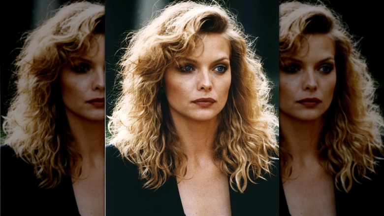 Michelle Pfeiffer with blond wavy hair unsmiling in low cut black top