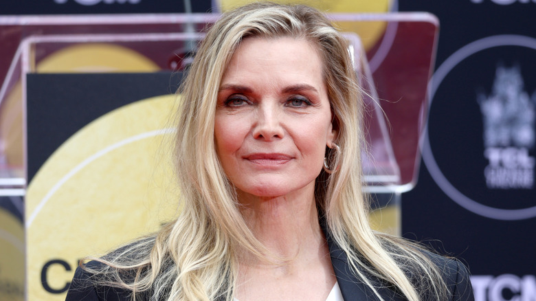 Michelle Pfeiffer with side parted hair in black blazer unsmiling