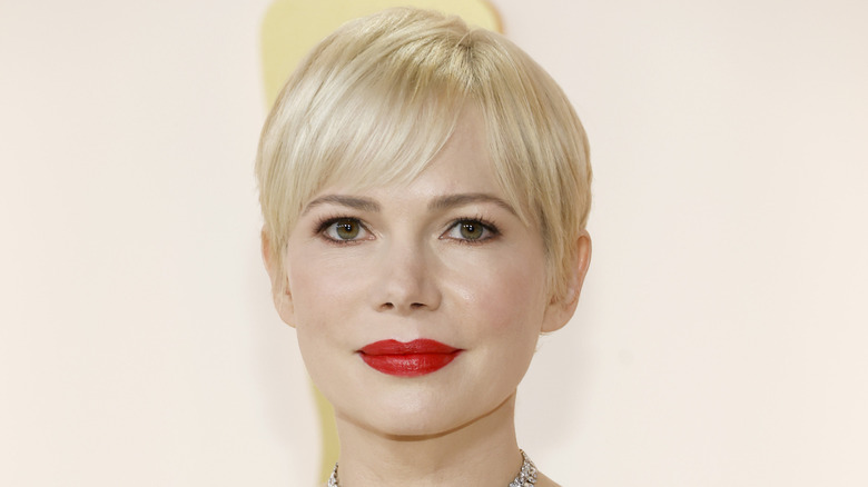 Closeup of Michelle Williams smiling with platinum blonde bob and a red lip.