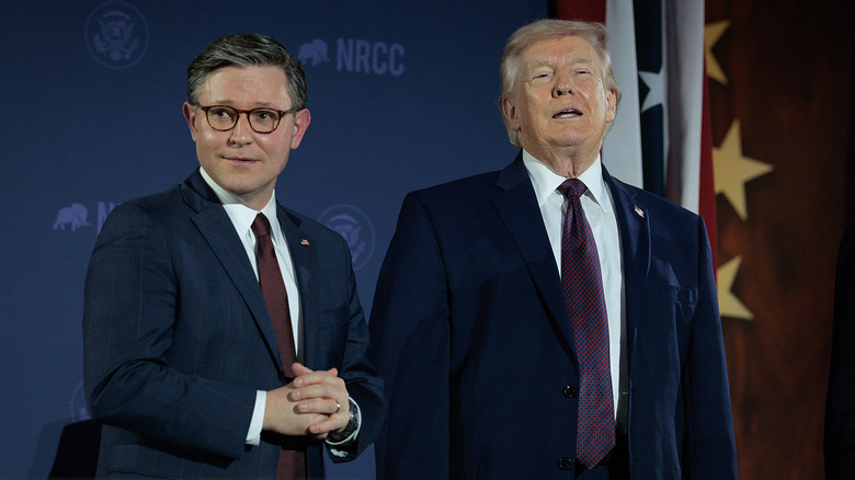 Mike Johnson clasping his hands while Donald Trump talks