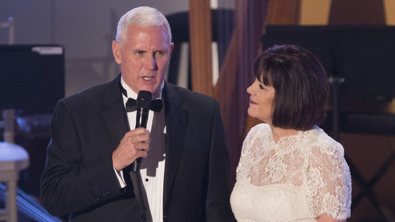 Mike Pence in a tux speaking into a microphone while Karen in a white dress looks on