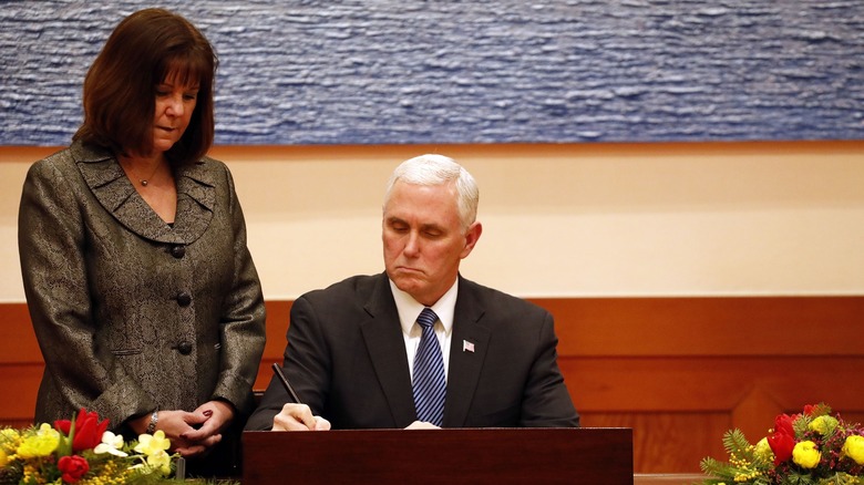 Karen Pence stands over Mike Pence while he signs something