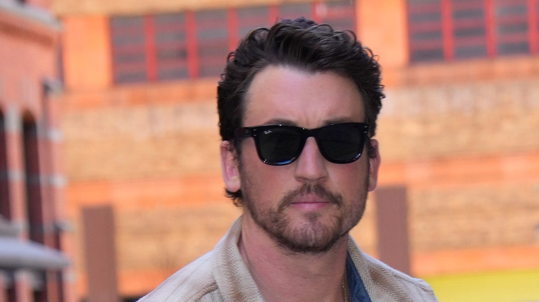 Miles Teller posing in a checked shirt and sunglasses