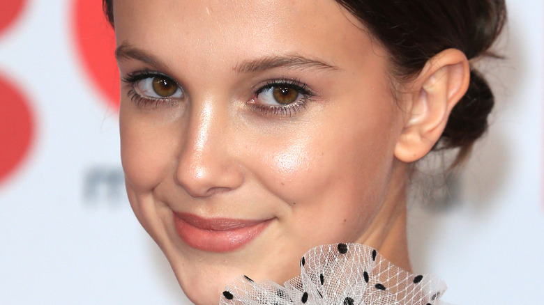 Millie Bobby Brown poses looking over her shoulder with a smile.