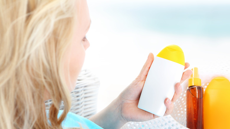 Blonde woman looking at sunscreen she's holding.