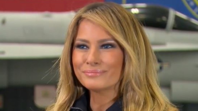 Melania Trump smiling in front of a plane