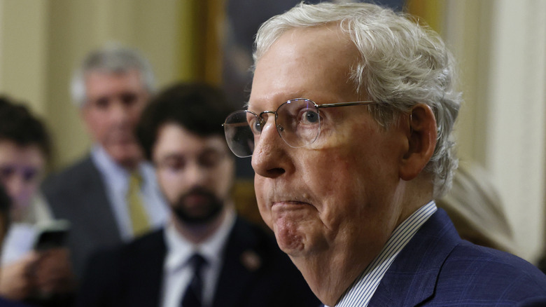 Mitch McConnell looking concerned while addressing the press with a frown