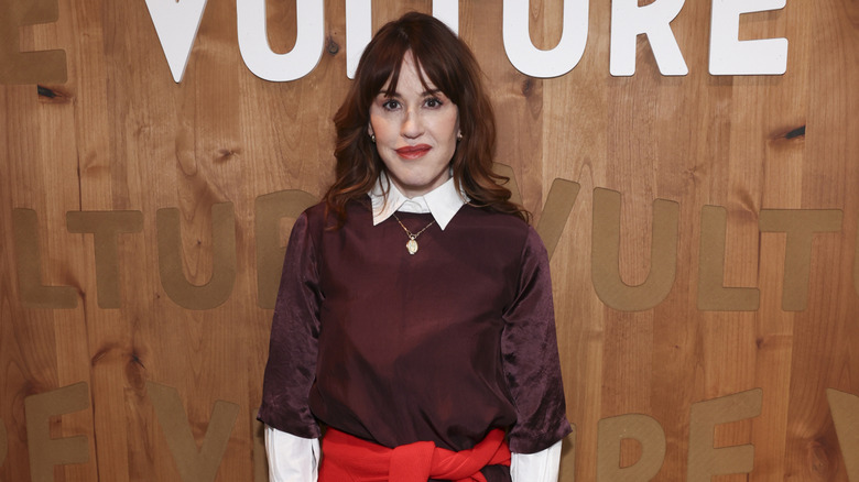 Molly Ringwald smiles in a maroon outfit