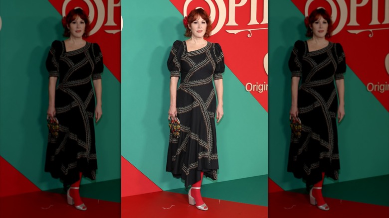 Molly Ringwald poses in a black dress and red tights
