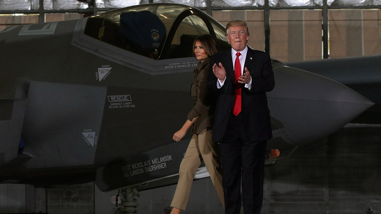 Donald Trumps claps in front of an F-35 fighter jet as Melania Trump walks behind him.