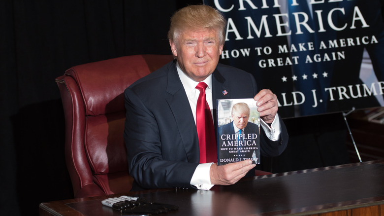 Donald Trump squints as he holds up his book "Crippled America."