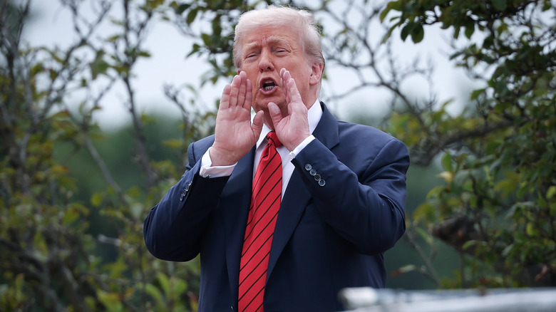 Donald Trump holds his hands up to his mouth to shout from the roof of the West Wing.