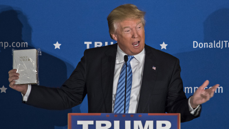 Donald Trump holds up a Bible wrapped in plastic with his arms outstretched.