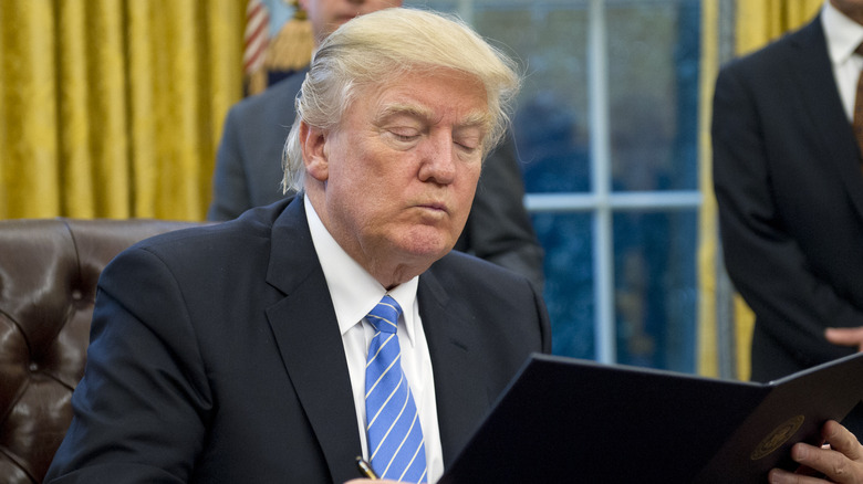 Donald Trump purses his lips while reading an executive order in the Oval Office.