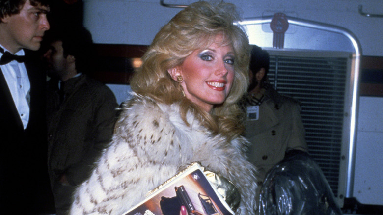 Morgan Fairchild with frosty eyeshadow, a red lip, and an extravagant fur coat walking through the streets of New York circa 1980