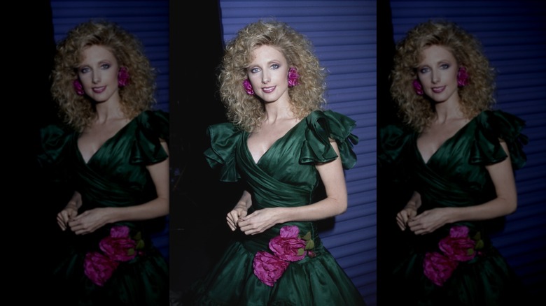 Morgan Fairchild in a puffy forest green dress with large magenta flower earrings with matching details on the drop waist of the dress