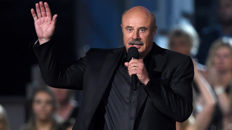 Dr. Phil delivering a speech with one hand raised, holding a mic in the other.