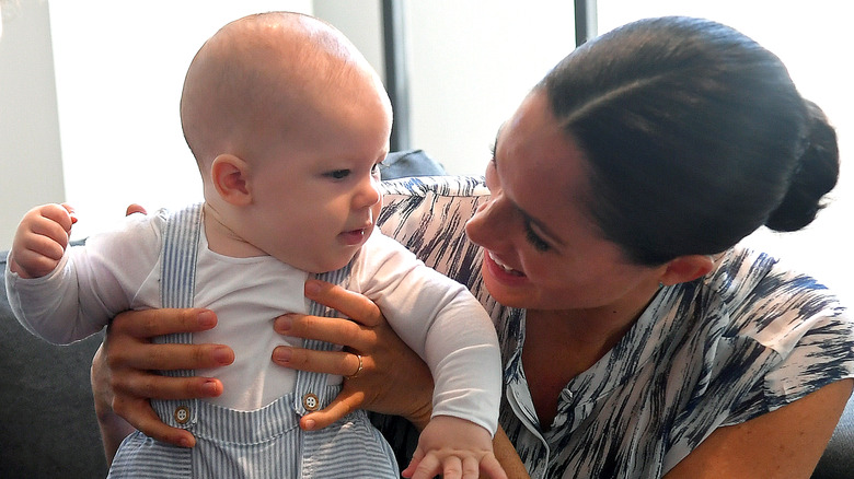 Meghan Markle holds up a young Prince Archie wearing baby clothes