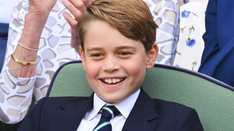 Prince George smiles from a seated arena at a sports match