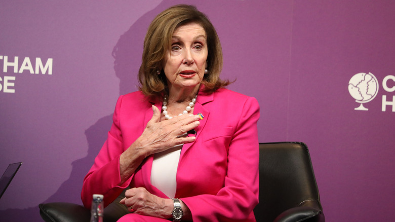 Nancy Pelosi holding her hand to her chest while speaking in a pink blazer