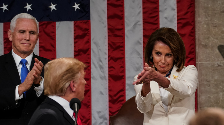 Nancy Pelosi clapping for Donald Trump next to Mike Pence in front of an American flag