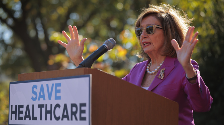 Nancy Pelosi giving a speech in a pink suit and sunglasses