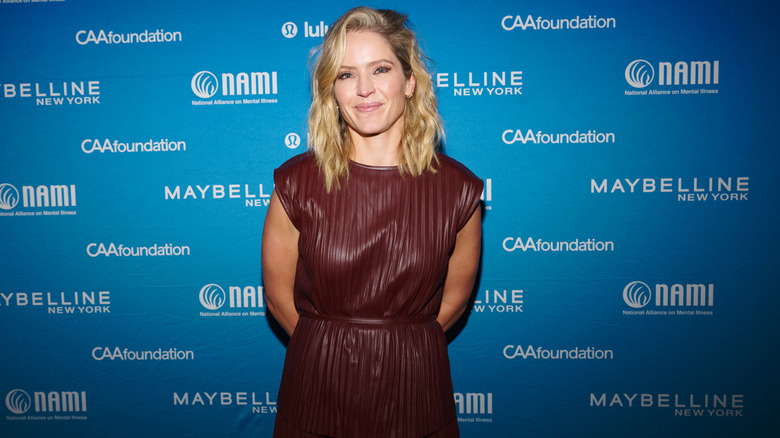 Sara Haines smiling on the red carpet with her hands behind her back in a brown leather dress