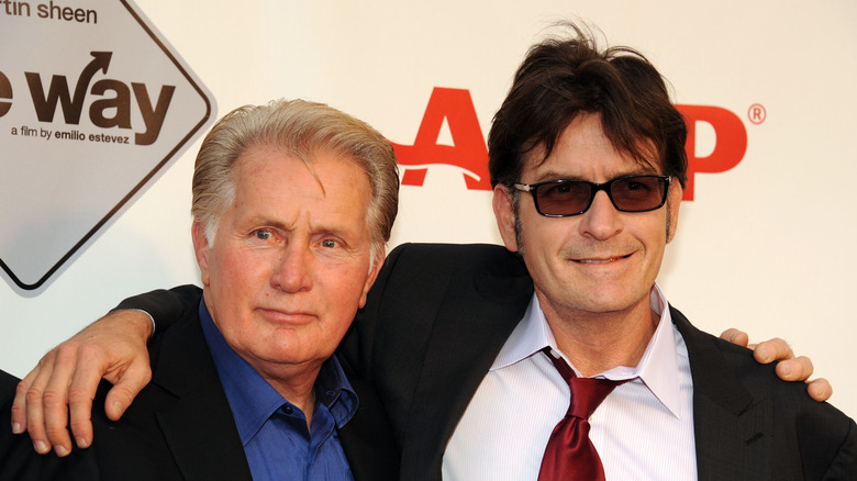 Charlie Sheen in black jacket, red tie, and sunglasses with dad Martin Sheen