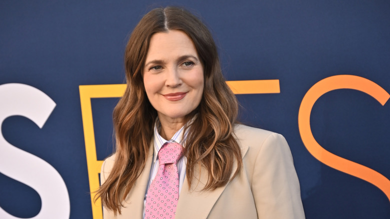 Drew Barrymore with dark hair in tan jacket and pink tie