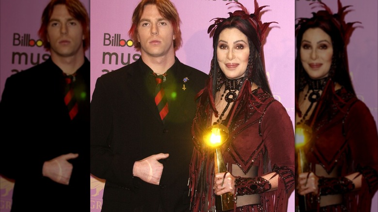 Elijah Blue Allman in black suit and striped tie with mom Cher holding award