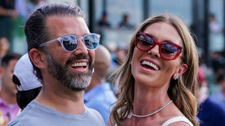 Donald Trump Jr. and Bettina Anderson wearing sunglasses and laughing.