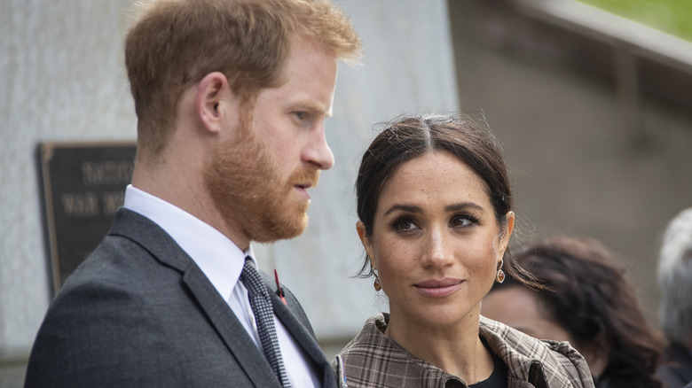 Prince Harry with serious expression, Meghan Markle looking at him