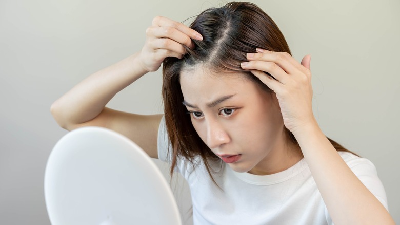 Woman looking in mirror at hair part