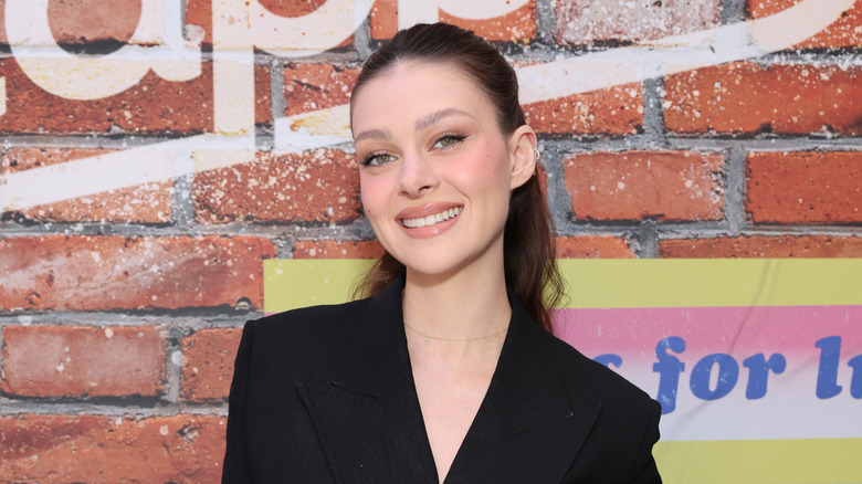 Nicola Peltz in a ponytail and black blazer smiling for a Snapple photo op