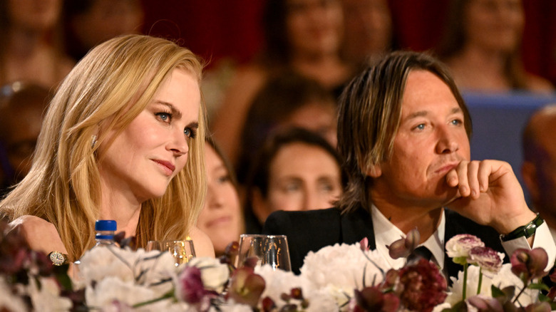 Nicole Kidman with her head titled sits beside Keith Urban who props his chin in his hand.